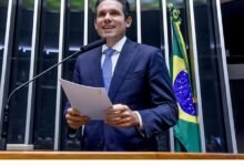 Quem é Hugo Motta discursando na Presidência da Câmara dos Deputados, segurando documentos diante da bandeira do Brasil.